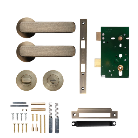 Door handle assembly with components on a white background. MomoAspenSolidBrassMorticeLockPrivacyLeverSetInDarkBrushedBrass